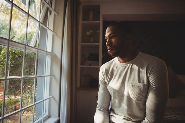 Thoughtful man sitting by window at home