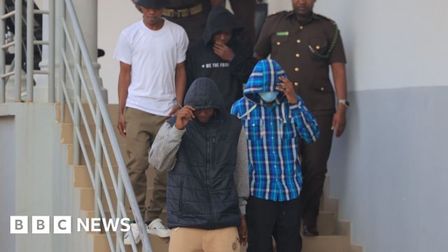 The four men convicted of rape walking down stairs, accompanied by prison officers
