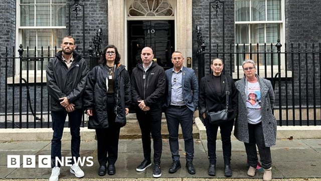 The families of the hostages standing outside the door of Downing Street - there are six people standing in a row with the famous black door behind them. Steve Brisley, Ayelet Svatitzky, and Sharone Lifschitz are all present, with a separate woman wearing a t-shirt with a picture of what is presumably her relative.
