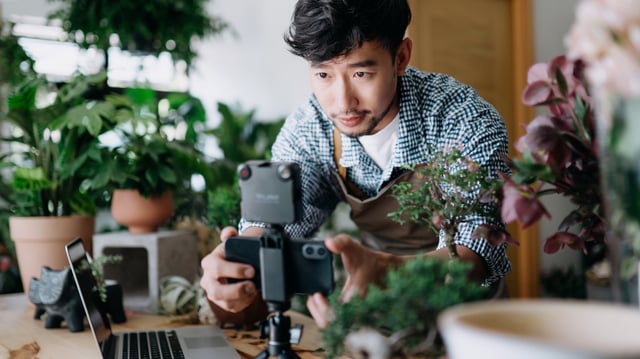 Man surrounded by plants filming on tripod