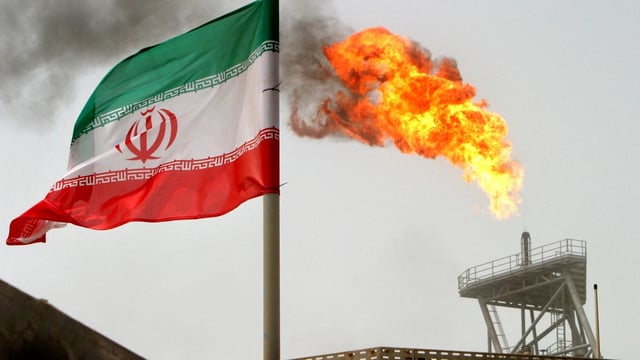 A gas flare is seen alongside an Iranian flag 