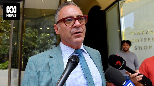 Andrew O'Keefe addresses the media wearing a suit and red glasses