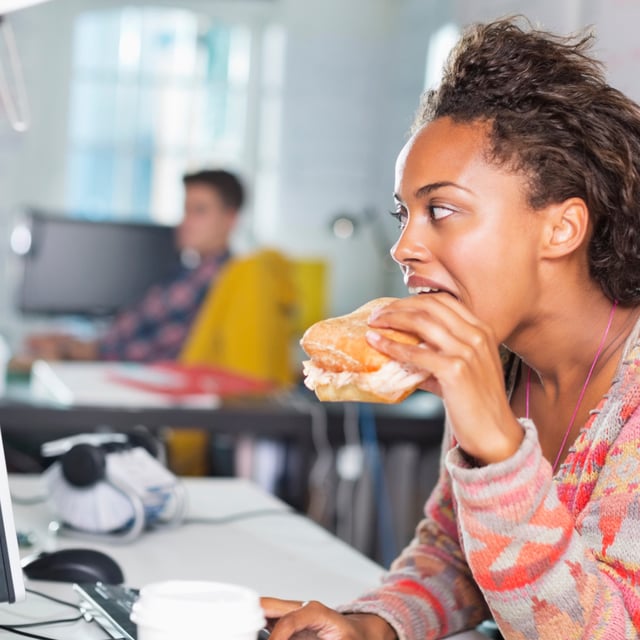 A file photo of a woman eating a burger at a desk. A survey has found that Gen Z feel guilty about taking lunch breaks.