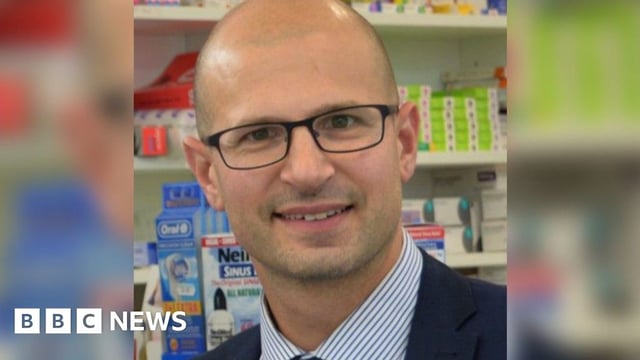Olivier Picard smiling at the camera, wearing dark framed glasses and a blue stripe shirt with navy blazer.