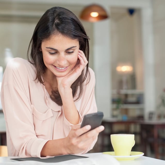 A woman drinking coffee in a yellow cup smiles while looking at her cell phone. Today's "Connections" game is hard, so if you're in need of some assistance, take a look at Newsweek's helpful clues.