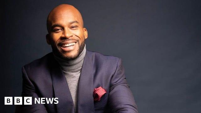 Dean Forbes dressed in a grey polo neck sweater and tailored suit