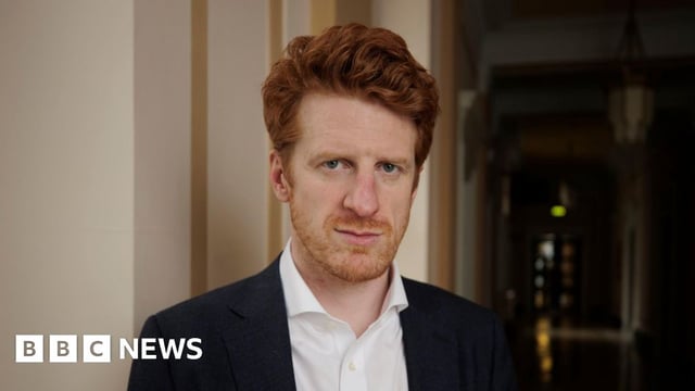 Matthew O'Toole wearing a black suit jacket and a white shirt. He has ginger hair and a ginger beard.