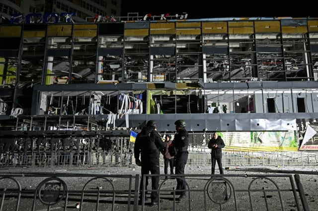 Ukrainian law enforcement officers stand next to a destroyed supermarket building following a missile attack in Kharkiv