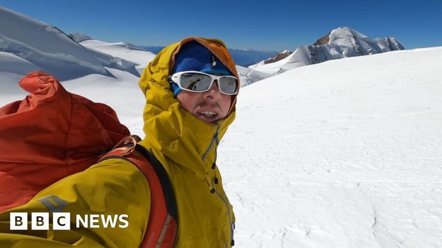 Ondrej Huserka dressed in yellow and wearing sunglasses, standing in snow-covered mountain landscape