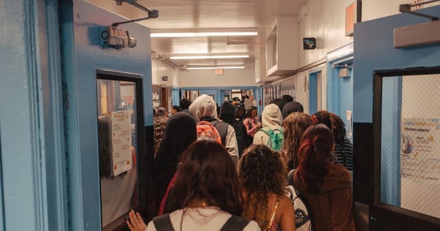 A group of high school students walk through a pair of blue doors.