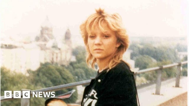 An old photograph of a young woman, standing on a balcony and looking at the camera. She has blonde hair and is wearing a black top.