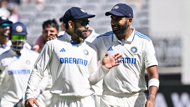 India's skipper Jasprit Bumrah (R) and Virat Kohli (L) speak as they walk back to the pavilion at the tea break on day four of the first Test cricket match between Australia and India