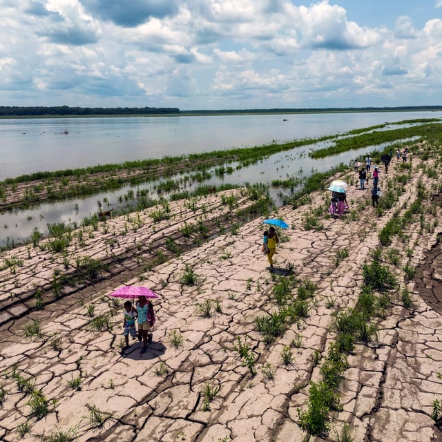 People walk through a part of the Amazon River that shows signs of drought in Santa Sofia, on the outskirts of Leticia, Colombia, on Oct. 20, 2024. (AP Photo/Ivan Valencia)