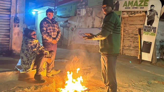 People stand close to the bonfire on a cold winter night at Madanpuri road near Hanuman Mandir, in Gurugram, India, on Sunday
