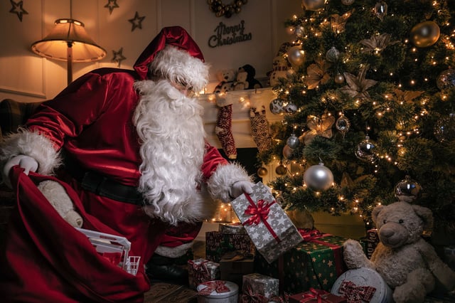 Santa Claus putting gifts under the christmas tree at night