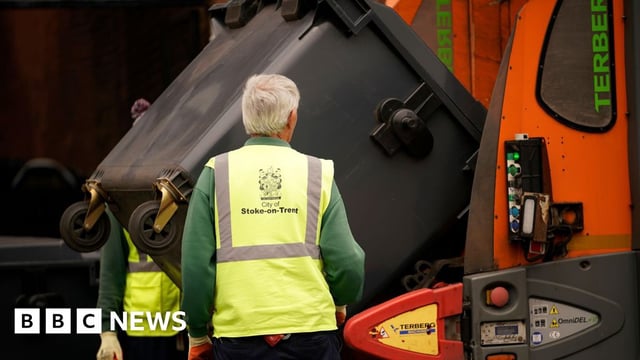 A bin lorry collects rubbish, flanked by two collectors wearing high-vis vests, in Stoke-on-Trent