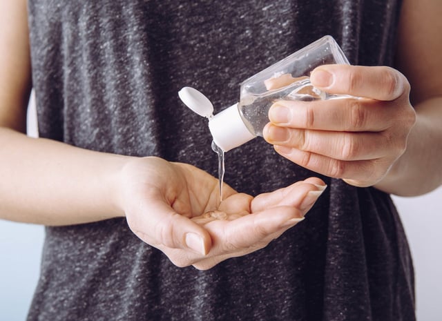 Woman uses a small portable antibacterial hand sanitizer on her hands.