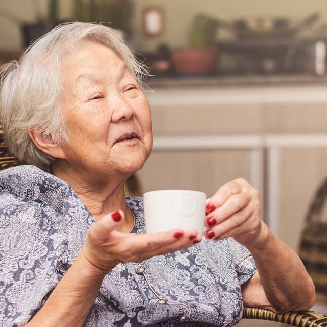 An old lady sits comfortably at home holding a cup of tea with a happy expression. Drinking more green tea might protect brain health due to its antioxidant and anti-inflammatory properties, Japanese scientists found.