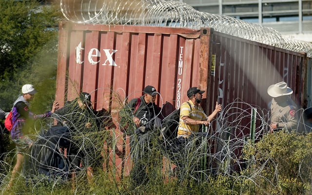 A Texas Department of Public Safety official, right, looks on as migrants walk near a rail car covered in Concertina wire at the Texas-Mexico border, Wednesday, Jan. 3, 2024, in Eagle Pass, Texas. U.S. House Speaker Mike Johnson is leading about 60 fellow Republicans in Congress on a visit to the Mexican border. Their trip comes as they are demanding hard-line immigration policies in exchange for backing President Joe Biden&#39;s emergency wartime funding request for Ukraine.