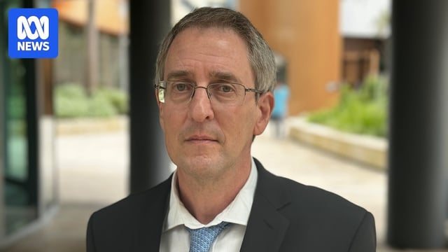 An older man looking dour while wearing a suit with a blue tie, and his top button undone