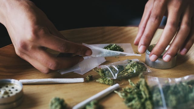 Cropped shot of a man rolling a marijuana joint at home