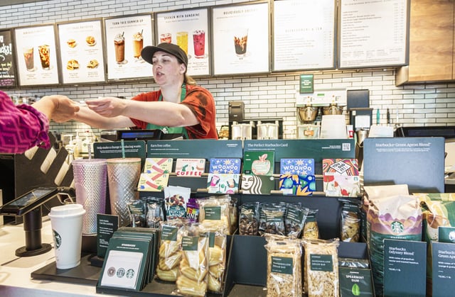 Starbucks Coffee barista handing drink and straw to customer.