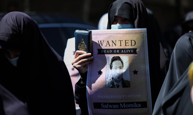 Des manifestants iraniens scandent des slogans tandis que l'un d'eux brandit un exemplaire du Coran, le livre sacré de l'islam, lors d'une manifestation contre l'incendie d'un Coran en Suède, devant l'ambassade de Suède à Téhéran, en Iran.