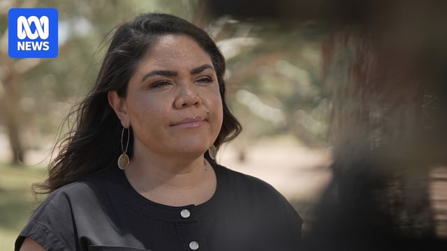 Woman stands in park with microphone in front of chest 