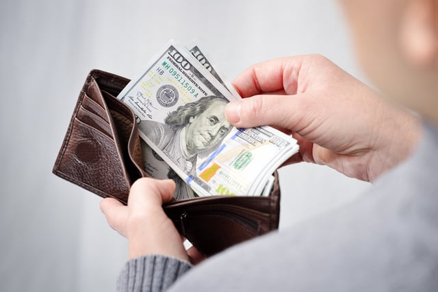 Stock image/file photo: A person taking U.S. Dollar bills out of a wallet.