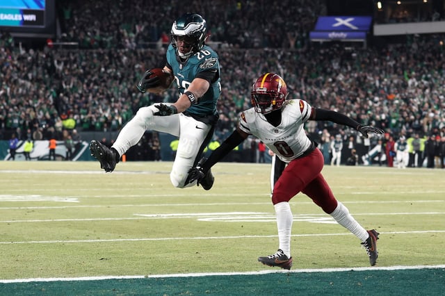PHILADELPHIA, PENNSYLVANIA - JANUARY 26: Saquon Barkley #26 of the Philadelphia Eagles scores a touchdown against Mike Sainristil #0 of the Washington Commanders during the fourth quarter in the NFC Championship Game at Lincoln Financial Field on January 26, 2025 in Philadelphia, Pennsylvania.