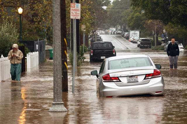 People gather along a flooded street as a powerful long-duration atmospheric river storm, the second in less than a week, impacts California on February 4, 2024, in Santa Barbara, California.
