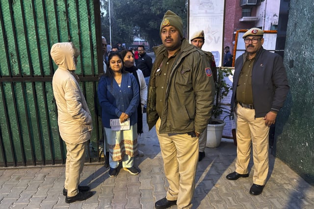 People stand in a queue to cast their votes for the capital’s state legislature election as policemen stand guard at a polling booth in New Delhi, India, Wednesday, Feb. 5, 2025. (AP Photo/Shonal Ganguly)