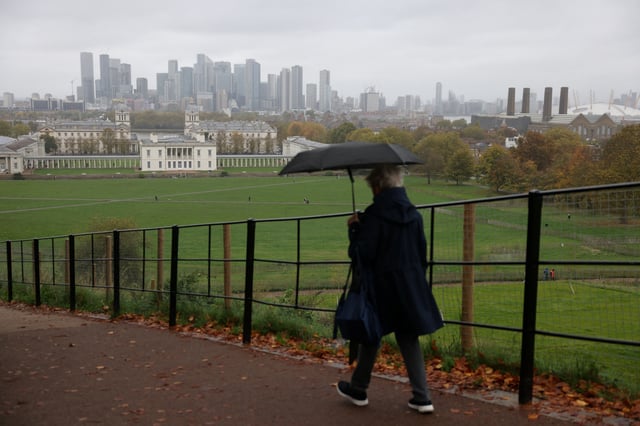 A woman holding an umbrella walks at Greenwich Park in view of the Canary Wharf skyline, in London, Britain, October 28, 2024. REUTERS/Hollie Adams/File Photo