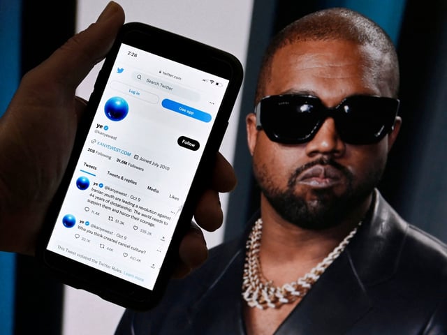 In this photo illustration, the Twitter account of Kanye West is displayed on a mobile phone with a photo of him shown in the background on October 28, 2022 in Washington, DC. - Rapper Kanye West's Twitter account, which was temporarily locked out after posting anti-Semitic remarks, appeared to be back up on the platform, on October 28 after billionaire Elon Musk took ownership of the social media company. (Photo by OLIVIER DOULIERY / AFP) (Photo by OLIVIER DOULIERY/AFP via Getty Images)