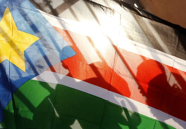 FILE - Southern Sudanese people are seen through a Southern Sudanese flag lining up to cast their votes in Juba, Southern Sudan, Jan. 9, 2011. (AP Photo/Jerome Delay, File)