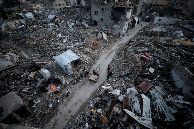 Palestinians gather near a fire next to the rubble of destroyed buildings, amid a ceasefire between Israel and Hamas, at Jabalia refugee camp, northern Gaza Strip, February 13, 2025. REUTERS/Mahmoud Issa