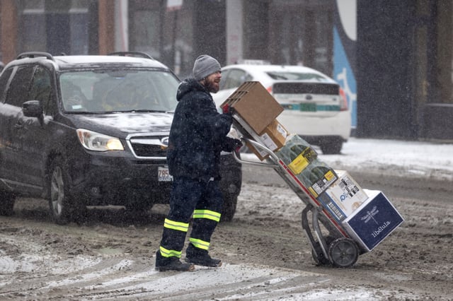 A worker pushes a delivery across a snow-covered street as a winter storm passes over the city on February 12, 2025 in Chicago, Illinois.