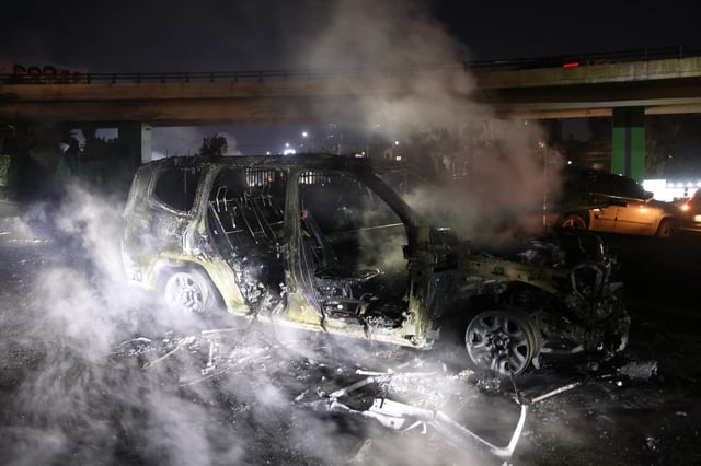 De la fumée s’échappe des restes brûlés d’un véhicule de la FINUL, incendié par des manifestants, sur la route menant à l’aéroport international de Beyrouth, le 14 février 2025.