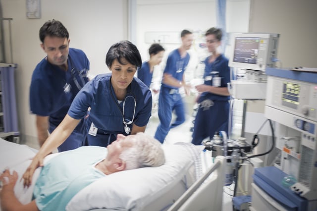 Stock image of a patient lying in bed in a busy hospital.