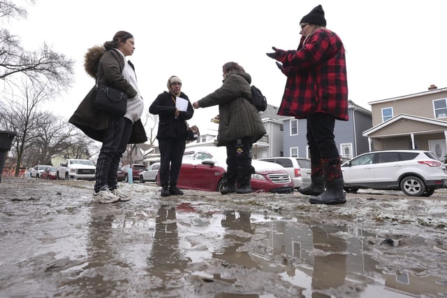 Neighbors talk on their mud covered street Wednesday, Feb. 19, 2025 after a recent water main break caused flooding in Detroit. (AP Photo/Paul Sancya)