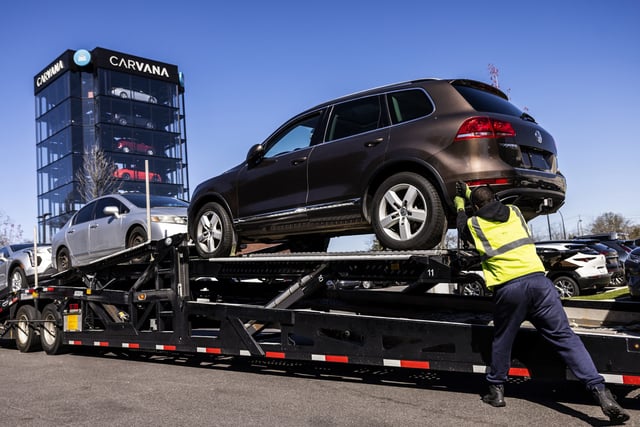 A worker loads vehicles onto a transporter at a Carvana vending machine location in Uniondale, N.Y., on April 16, 2024.
