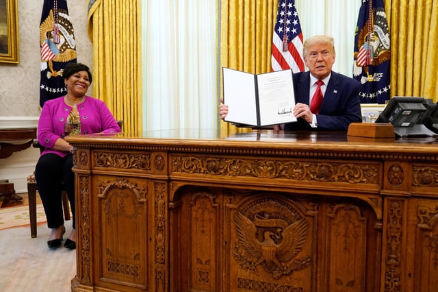President Donald Trump holds up a full pardon for Alice Marie Johnson in the Oval Office of the White House on Friday, Aug. 28, 2020.
