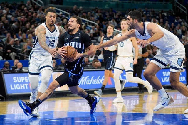 Magic guard Cole Anthony goes between Memphis forward Brandon Clarke (15) and center Zach Edey (right)  for a shot during the first half on Friday night at Kia Center. (AP Photo/John Raoux)