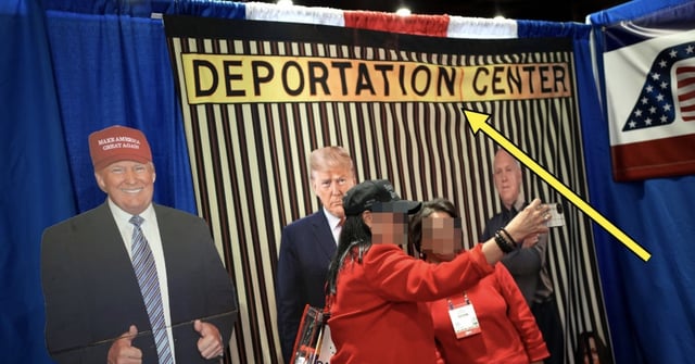 People take a selfie in front of a backdrop with political figures behind bars, labeled "Deportation Center," at a public event