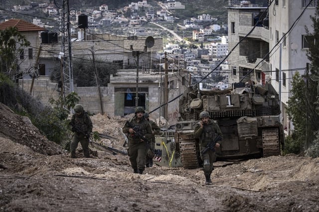 Des soldats israéliens marchent derrière un char dans le camp de réfugiés palestiniens de Jénine, en Cisjordanie occupée, lors d'une opération militaire, le 24 février 2025.