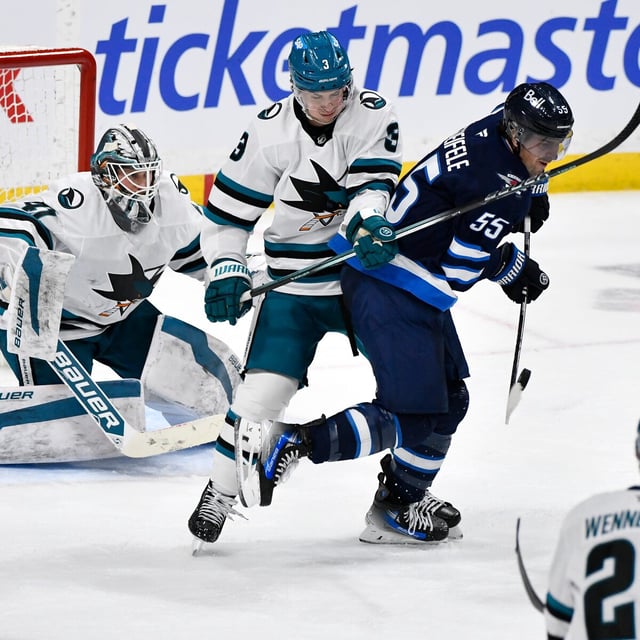 Winnipeg Jets' Mark Scheifele (55) deflects an incoming shot in front of San Jose Sharks goaltender Vitek Vanecek (41) and Henry Thrun (3) during third period NHL hockey action in Winnipeg, Monday, Feb. 24, 2025. THE CANADIAN PRESS/Fred Greenslade
