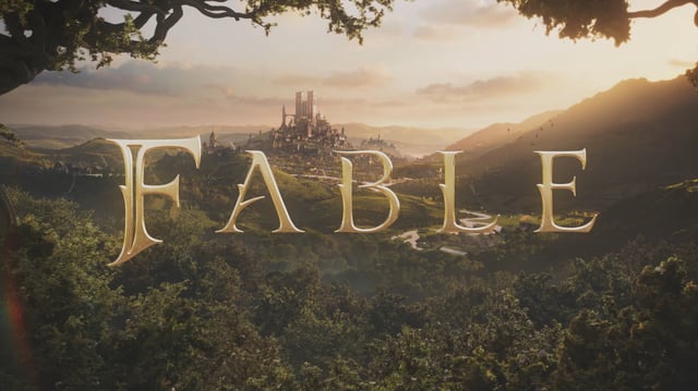 A golden &#34;Fable&#34; logo hovering in front of a vast landscape with a medieval township in the background.