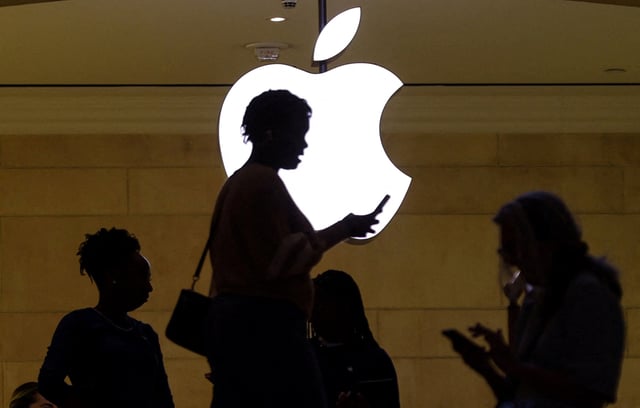A women uses an iPhone mobile device as she passes a lighted Apple logo at the Apple store at Grand Central Terminal in New York City, U.S., April 14, 2023. REUTERS/Mike Segar/File Photo