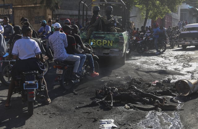 EDS NOTE: GRAPHIC CONTENT - Civilians and police officers drive past a charred body of suspected gang members set on fire by residents in Port-au-Prince, Haiti, Monday, Feb. 24, 2025. (AP Photo/Odelyn Joseph)