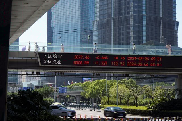 People walk on an overpass with a display of stock information in front of buildings in the Lujiazui financial district in Shanghai, China August 6, 2024. REUTERS/Nicoco Chan/File Photo